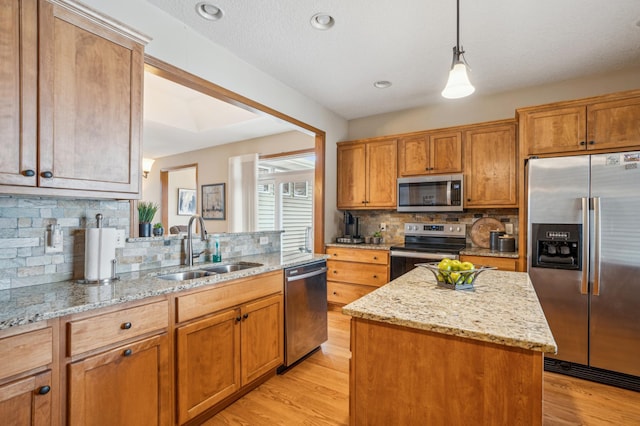 kitchen featuring appliances with stainless steel finishes, a sink, light wood-style flooring, a center island, and backsplash