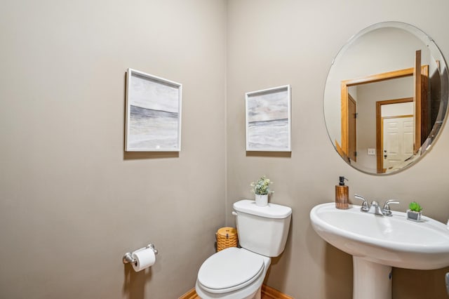 half bathroom featuring toilet, baseboards, and a sink