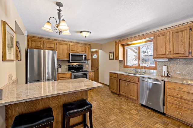 kitchen with a notable chandelier, a sink, a kitchen breakfast bar, appliances with stainless steel finishes, and a peninsula