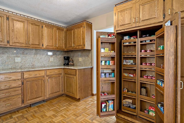 kitchen featuring backsplash, a textured ceiling, brown cabinets, and light stone countertops