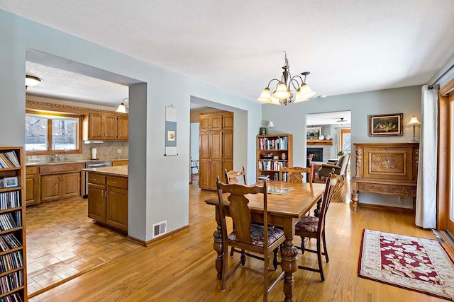 dining area with light wood-type flooring, visible vents, an inviting chandelier, a fireplace, and baseboards