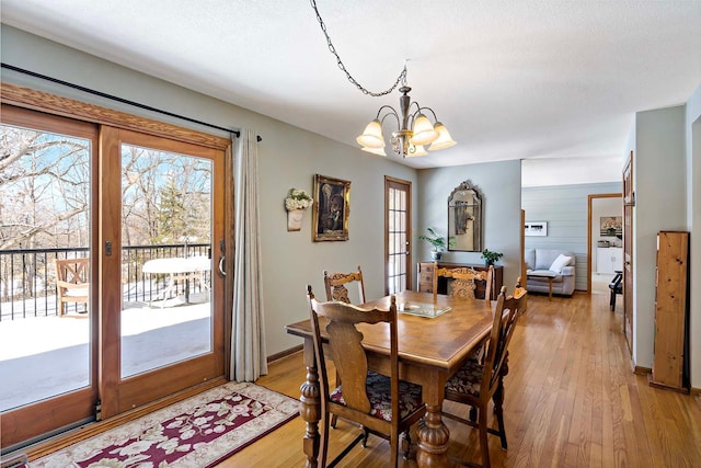 dining area featuring a notable chandelier, baseboards, light wood finished floors, and a textured ceiling