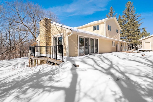 snow covered house featuring a deck and a chimney