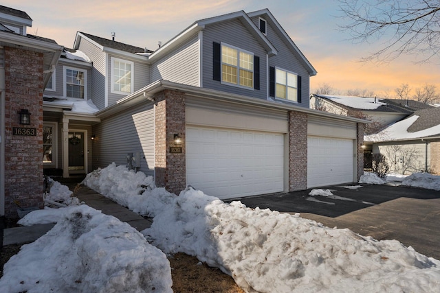 view of snowy exterior with aphalt driveway, stone siding, and a garage