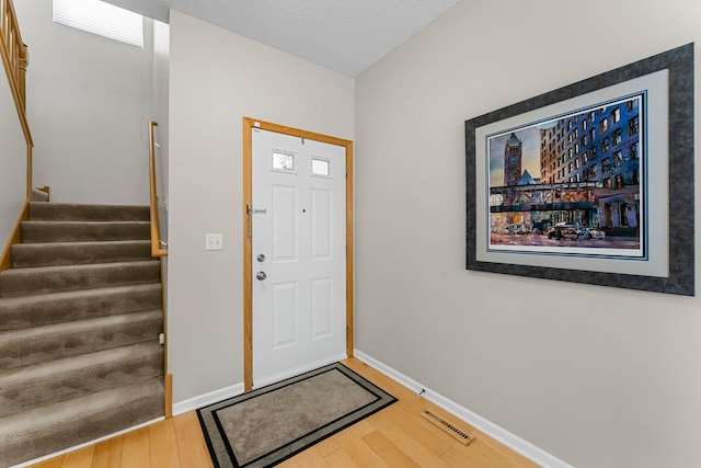 entrance foyer with visible vents, baseboards, wood finished floors, and stairs