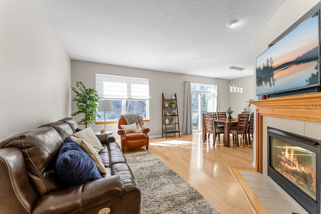 living area with a tiled fireplace, light wood-style floors, baseboards, and a textured ceiling