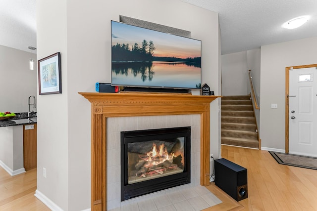 interior space with a tiled fireplace, wood finished floors, baseboards, and a textured ceiling