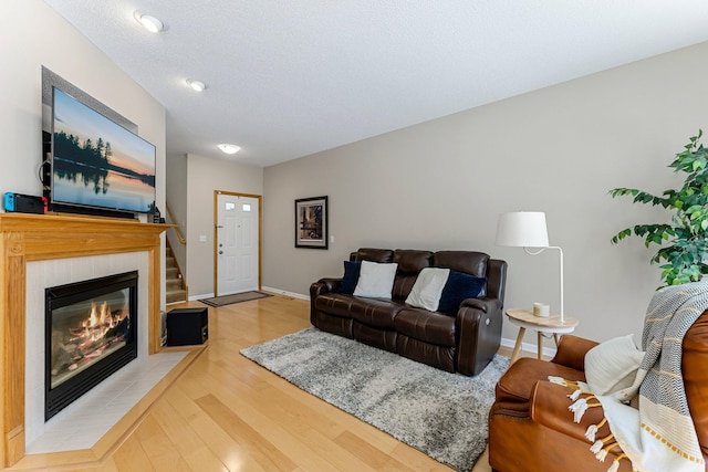 living area with baseboards, a textured ceiling, wood finished floors, and a tile fireplace