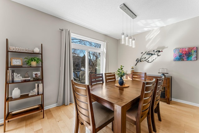 dining room with light wood-style flooring, baseboards, and a textured ceiling