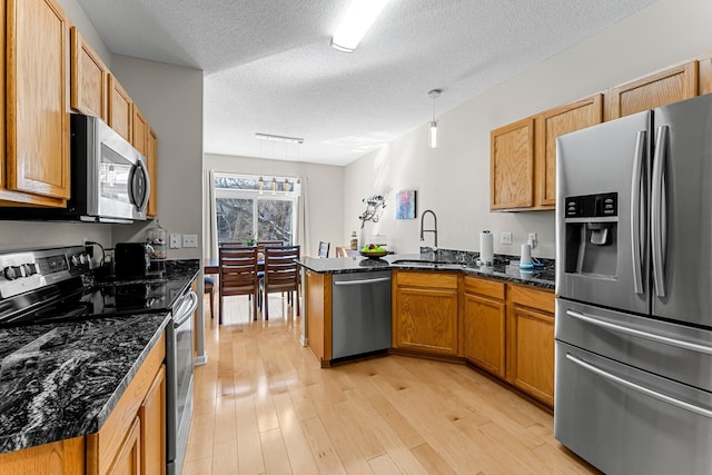 kitchen with a sink, dark stone countertops, stainless steel appliances, a peninsula, and light wood finished floors