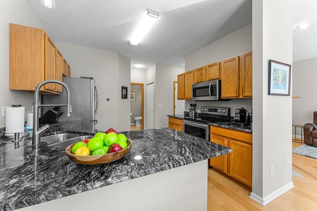 kitchen featuring dark stone countertops, a peninsula, a sink, stainless steel appliances, and light wood-type flooring