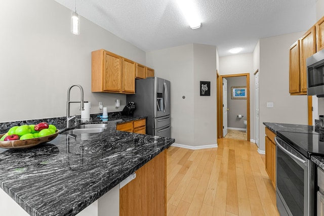 kitchen with light wood-style flooring, appliances with stainless steel finishes, a peninsula, a textured ceiling, and a sink