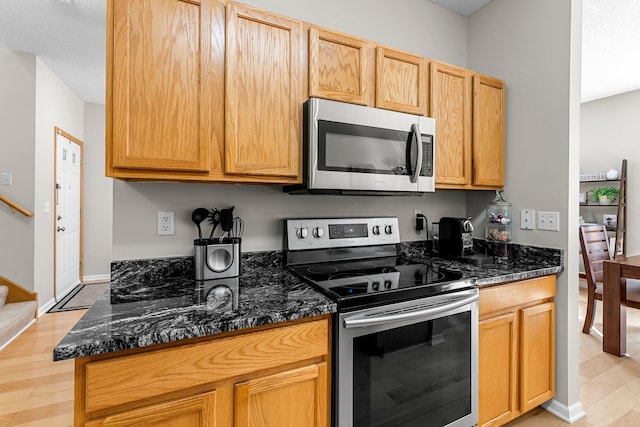 kitchen featuring dark stone counters, baseboards, light wood finished floors, and stainless steel appliances