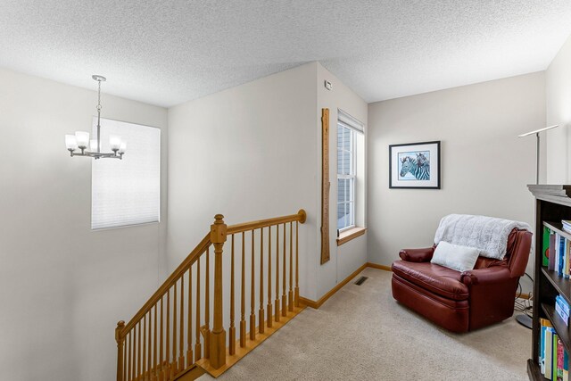 living area with baseboards, carpet floors, a textured ceiling, a notable chandelier, and an upstairs landing