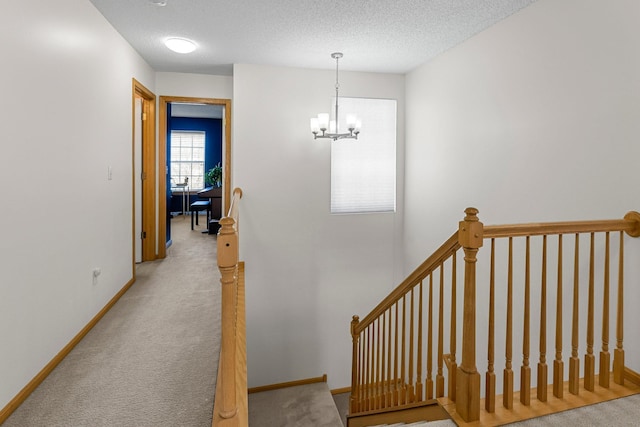 stairway featuring baseboards, a notable chandelier, carpet flooring, and a textured ceiling