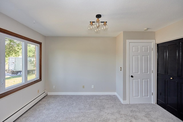 unfurnished room featuring light carpet, baseboard heating, a notable chandelier, and baseboards