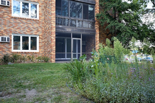 rear view of house featuring a sunroom, brick siding, a yard, and a wall mounted AC