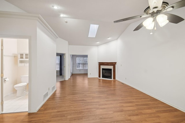 unfurnished living room featuring a fireplace with flush hearth, light wood-type flooring, visible vents, and lofted ceiling with skylight