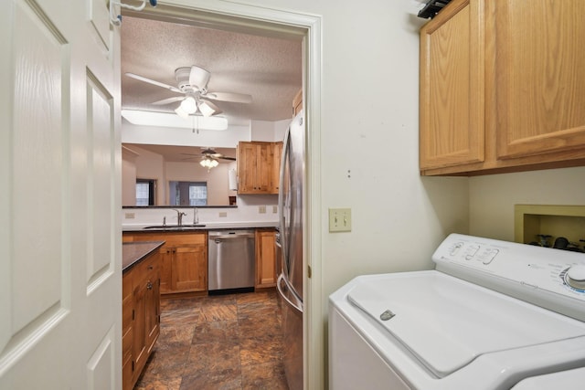 laundry room with a textured ceiling, a sink, cabinet space, stone finish floor, and washer / dryer