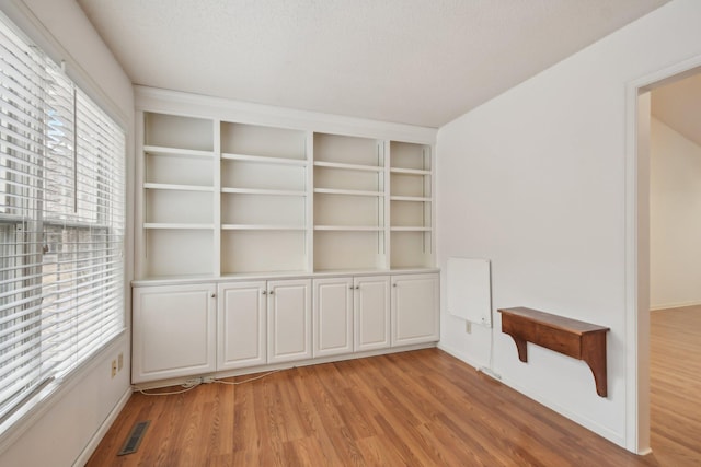 unfurnished room with light wood-type flooring, a textured ceiling, visible vents, and a wealth of natural light