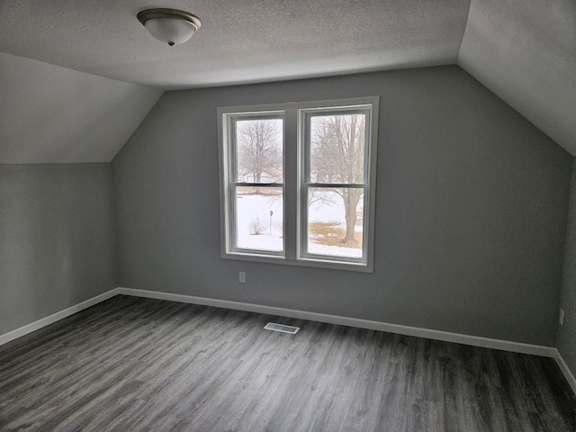 additional living space with baseboards, a textured ceiling, visible vents, and dark wood-style flooring