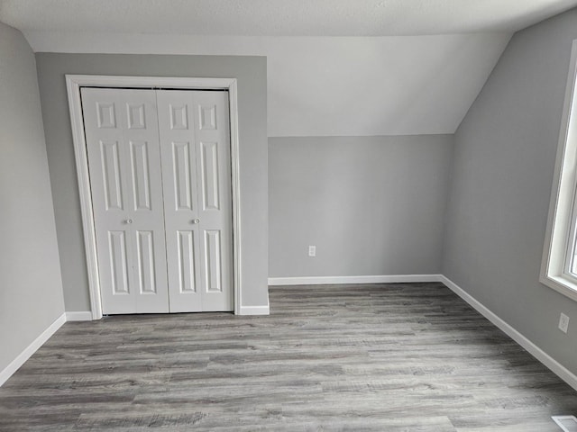 interior space featuring light wood-type flooring, a closet, lofted ceiling, and baseboards