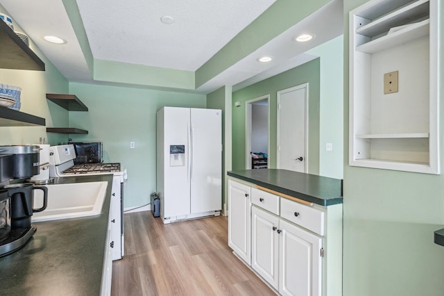 kitchen featuring white appliances, light wood finished floors, white cabinets, dark countertops, and open shelves