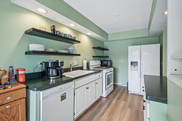 kitchen featuring white appliances, a sink, white cabinets, open shelves, and dark countertops