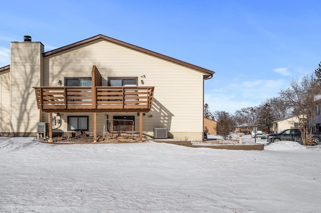 snow covered property with central AC, a chimney, and a wooden deck