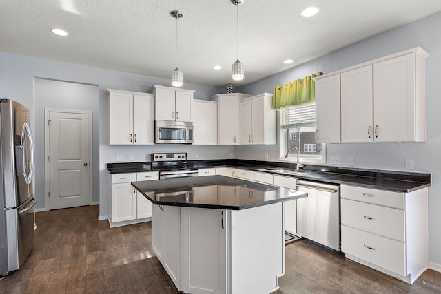 kitchen with stainless steel appliances, dark countertops, a sink, and white cabinetry