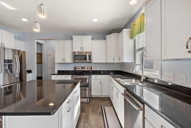 kitchen featuring dark wood finished floors, white cabinets, appliances with stainless steel finishes, decorative light fixtures, and a sink