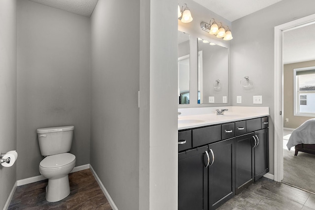 ensuite bathroom with baseboards, a sink, toilet, and double vanity