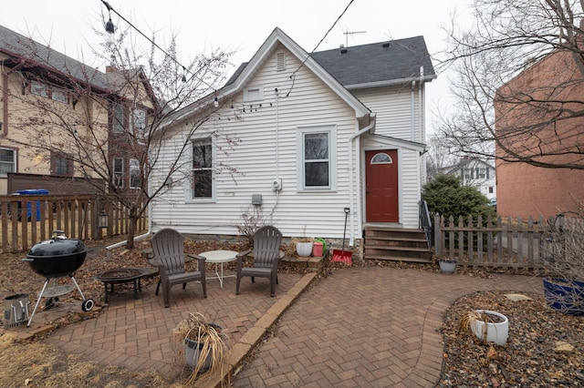 rear view of property featuring a shingled roof, an outdoor fire pit, a patio area, and fence