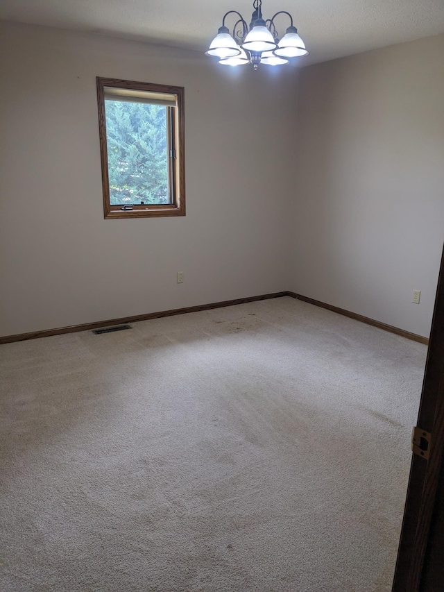 spare room with carpet floors, visible vents, a notable chandelier, and baseboards