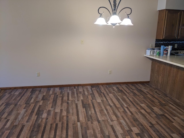 unfurnished dining area featuring a chandelier, dark wood-type flooring, and baseboards