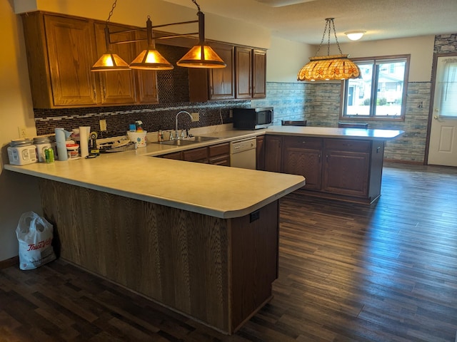 kitchen featuring stainless steel microwave, a peninsula, white dishwasher, light countertops, and a sink