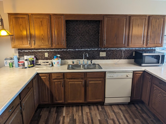 kitchen with light countertops, stainless steel microwave, dark wood-type flooring, white dishwasher, and a sink