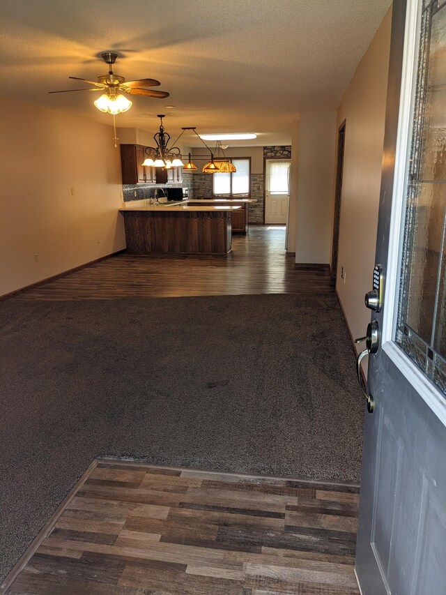 kitchen with a peninsula, open floor plan, dark colored carpet, dark wood finished floors, and pendant lighting