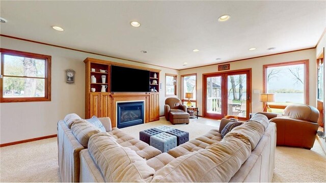 living area with baseboards, a glass covered fireplace, light colored carpet, ornamental molding, and recessed lighting