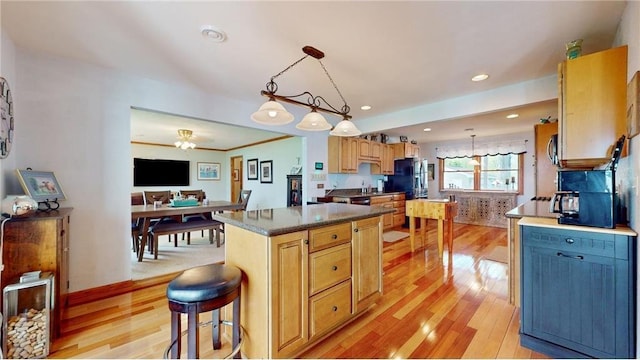 kitchen featuring a center island, decorative light fixtures, dark countertops, light wood-type flooring, and a kitchen breakfast bar