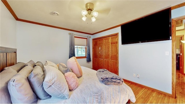 bedroom featuring baseboards, a ceiling fan, light wood-style flooring, crown molding, and a closet