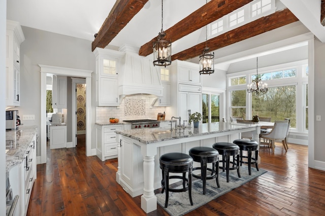 kitchen featuring stove, white cabinetry, custom range hood, decorative backsplash, and an inviting chandelier