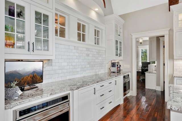 kitchen featuring decorative backsplash, dark wood-type flooring, white cabinets, stainless steel oven, and light stone countertops