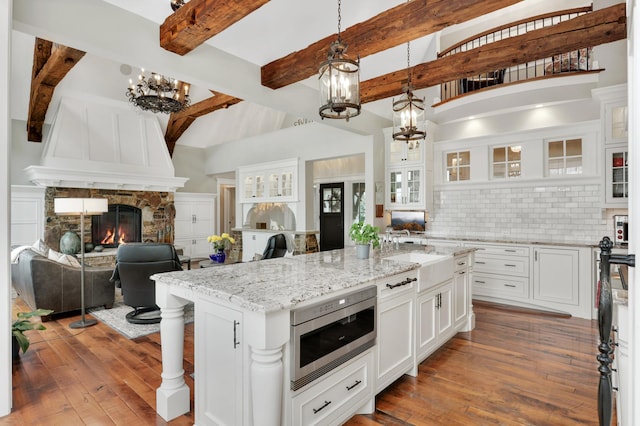 kitchen with a notable chandelier, stainless steel microwave, a sink, a stone fireplace, and hardwood / wood-style floors