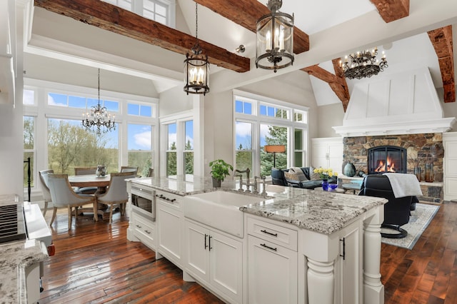 kitchen with stainless steel microwave, light stone countertops, a stone fireplace, a chandelier, and a sink