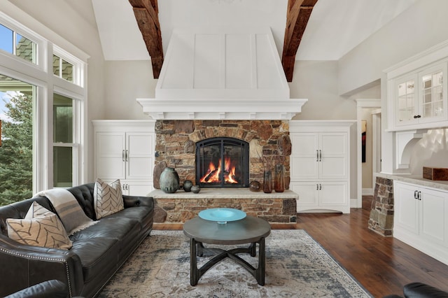 living room with vaulted ceiling with beams, dark wood-style floors, and a stone fireplace