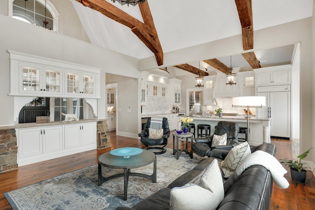 living area with dark wood-type flooring, beam ceiling, a notable chandelier, and baseboards