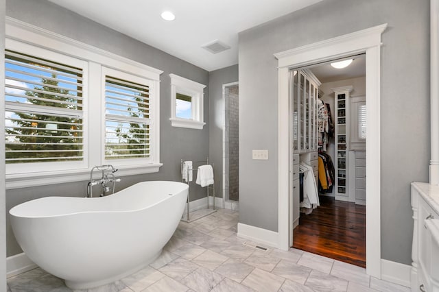 bathroom featuring a walk in closet, a freestanding tub, marble finish floor, and baseboards