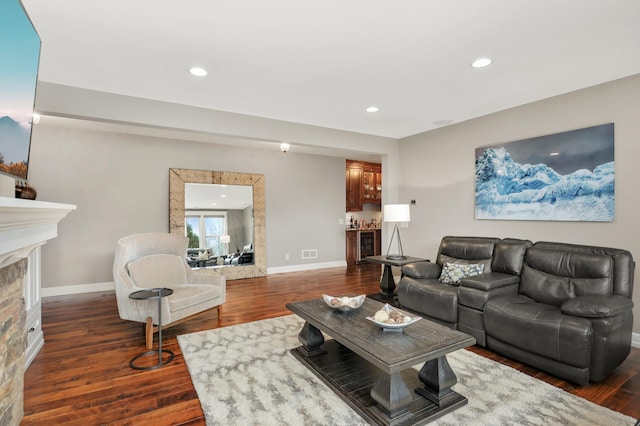 living area featuring recessed lighting, baseboards, dark wood-type flooring, and a stone fireplace