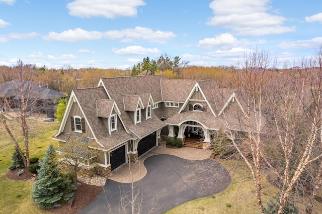 view of front of home featuring stone siding, aphalt driveway, and roof with shingles